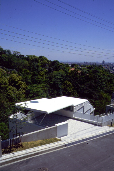 Glider House／苦楽園G9 フォルムのイメージは、山あいの谷間から、静かに風を切り飛び立とうとしているグライダーの翼から始まり、軽やかな構造の屋根で浮遊間を持たせた。雑木の敷地に埋没させようと考え、植栽用土面を残し、谷筋の方向に配した。全体は、階段によって、縦の連続性と内外の回遊性を計った。道路から玄関ホールへ潜り込み、谷間から広がる眺望開ける居間、食堂へと続く。最下層部には、最も自然に近い場所にタイル張りのテラスがある。そして、この上下階に挟まれて、少々閉ざされ色と光が抑制された個室群がある。<br /><br />