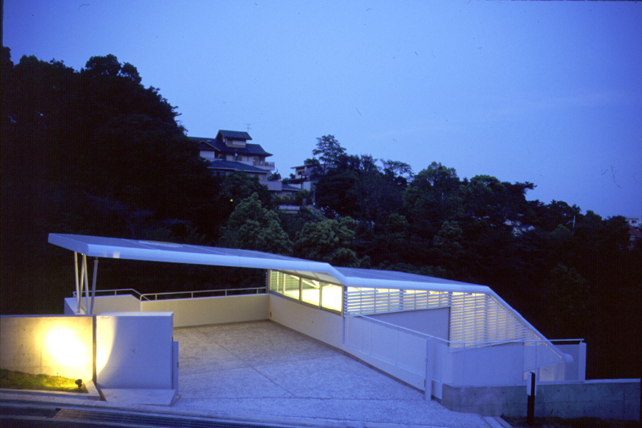 Glider House／苦楽園G9 フォルムのイメージは、山あいの谷間から、静かに風を切り飛び立とうとしているグライダーの翼から始まり、軽やかな構造の屋根で浮遊間を持たせた。雑木の敷地に埋没させようと考え、植栽用土面を残し、谷筋の方向に配した。全体は、階段によって、縦の連続性と内外の回遊性を計った。道路から玄関ホールへ潜り込み、谷間から広がる眺望開ける居間、食堂へと続く。最下層部には、最も自然に近い場所にタイル張りのテラスがある。そして、この上下階に挟まれて、少々閉ざされ色と光が抑制された個室群がある。<br /><br />