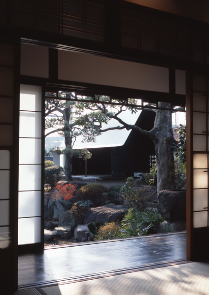 Steel Sheet Teahouse The engawa (veranda) in this minka faces the remnants of a precious Japanese-style garden, which was maintained for many years as a hobby of the preceding generation. Inheriting the shape of this bequest, a contemporary monocoque tearoom was newly installed in the garden. So as not to hurt the existing delicate garden trees, the main body of the tearoom was made in a factory, then simply placed in its location in the garden. Overall, it is divided into a half-exterior meeting part and a stoic interior space comprising an alcove and two tatami mats, covered with a roof membrane of steel sheet. An extraordinary space, this tearoom is a contemporary meditation space, and at the seasons change it is a place in dialogue with nature. As well as being also to wander through the exciting garden, visually there emerges a spatial continuity that unifies inside and outside even more than the engawa, producing a lifestyle in intimate contact with nature.<br /><br />The steel sheet that I used goes from an architectural building frame to an industrially processed product like a vehicle, and the sculptural usage avoids the impact of the strong expression of steel. The advantage of this material is its high degree of strength and the possibility of high-precision factory fabrication through using CAD; a standard quality may be maintained everywhere, the price-per-weight does not vary much, and it can cope with customization and prefabrication. The sizes for this tearoom were determined by the volume of heights and widths that are able to be transported by vehicle. It was all produced at the factory, and the 9mm-thick steel sheets were bent into curved surface at key points in order to make a unified pre-strengthened structure. Divided into two parts, it was then lowered as-it into the garden by crane. It was then reconnected, fittings were inserted, tatami mats were laid, and this was all completed over a short period of time. The inside and outside have been given a different expression. Traces of the fabrication process and welding have been left in the interior, and the outside is finished with industrial smooth painting like a vehicle, with a taste for simplicity and quiet.