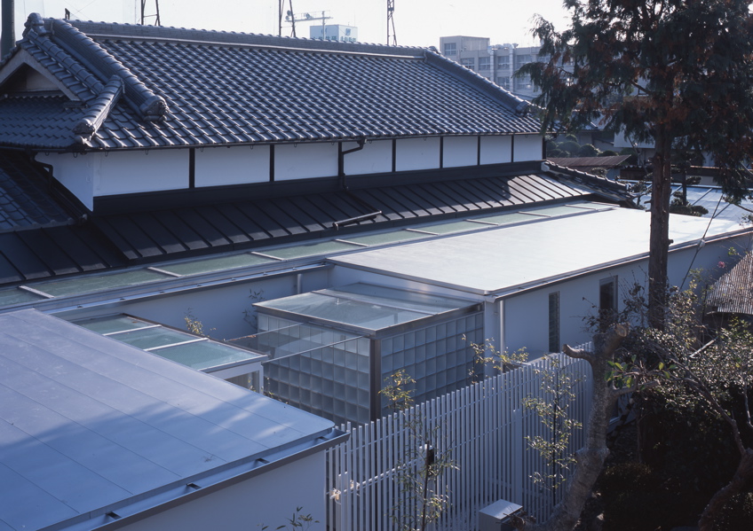 鉄の民家 この民家は、大阪近郊に残っていた貴重な民家である。これまで、幾度となく増改築が行われ、骨格と外観正面を除けば原型をとどめず、室内も新建材で改装されてしまっていた。残された資料も無く、建築主の記憶の聞き取りと建物調査から、増改築の痕跡を探り原型の復元に努めた。建設年代は、屋根裏から御弊が発見され、上棟は大正14年（1925年）11月とわかり、そして、古い土壁に貼られた昭和4年の新聞片も発見された。その壁面はガラスで覆い「痕跡」として保存した。全体は、改修と補強を行ったこの原型となる民家部分と、新たに改修築したスチール・シートで包まれた寝室とサニタリー部分、そして、和室の庭に設けられた小さな離家の茶室の3つに区分することができる。そして、この民家の木造部分とスチール・シートによって改修築された部分の間に、トップライトのある通り土間廊下を土間のリビング＋キッチンを設けた。このインターフェイスとしての土間空間を挿入することによって、環境調整を伴う光と風抜きのパッシブ的役割も担い、また、空間の新旧のメリハリと分節しながらも全体の各室を結び付け、昔乍らの和の生活と現代生活をうまく融合し、蘇生できたと考えている。<br /><br />スチール・シートによって改修築された部分は、t=9mmのスチール・シートで寝室とサニタリーを包むように囲っている。長筒状のフラットルーフの形状で、木造の民家部分とは対照的に車両が停車したように見える。既存の柱梁を取り替え、スチール・シートによって補強し、既存の柱間と合わせた半間間隔（960mm）にアングル型鋼をリブ状に建て、それを溝型鋼で門型につなぎ連続させている。この工法は、鉄船舶の居住部などを建造する工法と同じで、建築が柱梁に頼らない、より軽快なリブ構造によってモノコック建築の試みである。そして、土間廊下は、構造的緩衝体となり、民家部分の木造とこのモノコックの異種構造を力の伝達の少ないトップライトで繋いでいる。全体のディテールは、空間に突起部分のないできるだけ平滑でスッキリと格納した、何でない納まりとなるように考えた。