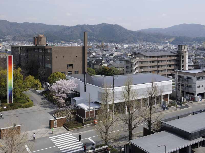 京都工芸繊維大学創立60周年記念館 ６０周年記念館は、シンボル的存在として大学中央口前に建つ。大学キャンバス計画に基づき、既存校舎の軸線に合わせ、既存樹木帯を残した外部道路との間に位置している。全体は、一階にメモリアルホール、ギャラリーと記念講義室があり、二階に大小のセミナーホールとそのホワイエラウンジがある。そして、一部構内の外構塀を取払い、直接外部道路からの使用可能な学外に開いた施設である。<br />記念館の構想にあたり、時間をテーマに記憶と時を静止させた時代を再確認する静的な建築であると捕らえた。建築は、過去から継承され失われる技術もあり、当然ながら機能では定まらず、感性、記憶、象徴等と多重的要素で成立している。<br />本大学創設当時の本野清吾設計による校舎は、やや重量感のあるRC造の建築であるが、しかし、W. Gropiusのドイツ工作連盟の透明感のあるFagus FactoryやBauhaus Buildingを想起させる新時代の建築であり、一時代の大学のシンボルとしてあり、当時のデザインスクールとして新たな近代デザインへの可能性を具現且つ体感的に示したものであった。<br />現代建築は、存在性が薄れつつある。しかしながら、建設に携わった職人達の無名の熟練した手の痕跡や建築素材により、建築そのものに命を与え、その空間体感が五感を呼び起こし、人に感動と敬意を促す。此れまで出会ったすばらしい建築は、それらが身体にダイレクトに伝わるものであった。そして、その時代の文化の結晶として残るのである。ここでは、そんな建築への思いと取り組み、空間の素材とディテールを熟考し、現代性の表現として鉄を使い、創設期の本野清吾のRC造の校舎と対称させた。<br />また、その表現として、空間の初原的な型としてのボルト架構の、２つの異なる相対によって、エレガント性とダイナミズム、そして、空間の格式と品格、更には、未来への可能性を暗示出来ればと考えた。