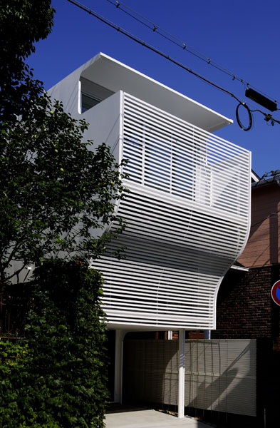 Steel Wall This small residential building is located in Hanshin area, a minute walk from nearby station. The site area is approximately 69m2. It is a town house designed for a young family. The lot is 4.5 metres in width and 50 metres in depth. The west side of the plot faces a street, and the south side faces an adjacent building. There is a height restriction of 5 metres for the north side of the lot, however this side enjoys the view of the vegetation from the adjacent residence. The east side faces a waterway. <br />South and north sides of the house are enclosed by plane walls with few small openings for ventilation purposes in order to avoid being seen by the neighbors. Contrastively, east and west sides are fully glazed. The building also takes light from the atrium and the roof top terrace. <br /> The ground floor consists of master bedroom which is connected to outside through doma (a space situated at the same level as the ground comprising the entrance hall). The first floor consists of children’s room, kitchen and bathroom. The upmost floor consists of a living room where is possible for all family members to gather. The building shape is planned so to realize the maximum possible size despite the height restriction. Continuity between inside and out is realized by locating balconies on the east and west sides connected to the atrium and the rooftop balcony. In this house, inside becomes essentially just another outside.<br />The vertical connection between the entrance hall and the rooftop terrace is seamlessly continuous. This house is like a minivan that accommodates a family. The title of this work “steel wall” is given by the fact that there are two load-bearing walls that carries the horizontal forces acting in transverse direction. They are located symbolically at the centre of the building and give continuity to architectural design with other structural members such as the mesh walls supporting the steel staircase as well as the texture of steel.<br />